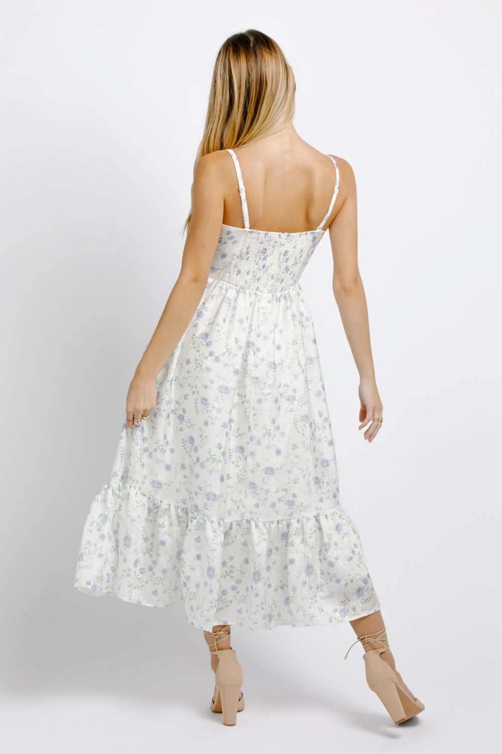 Back view of a woman wearing a white and blue floral dress on a plain background