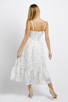 Back view of a woman wearing a white and blue floral dress on a plain background