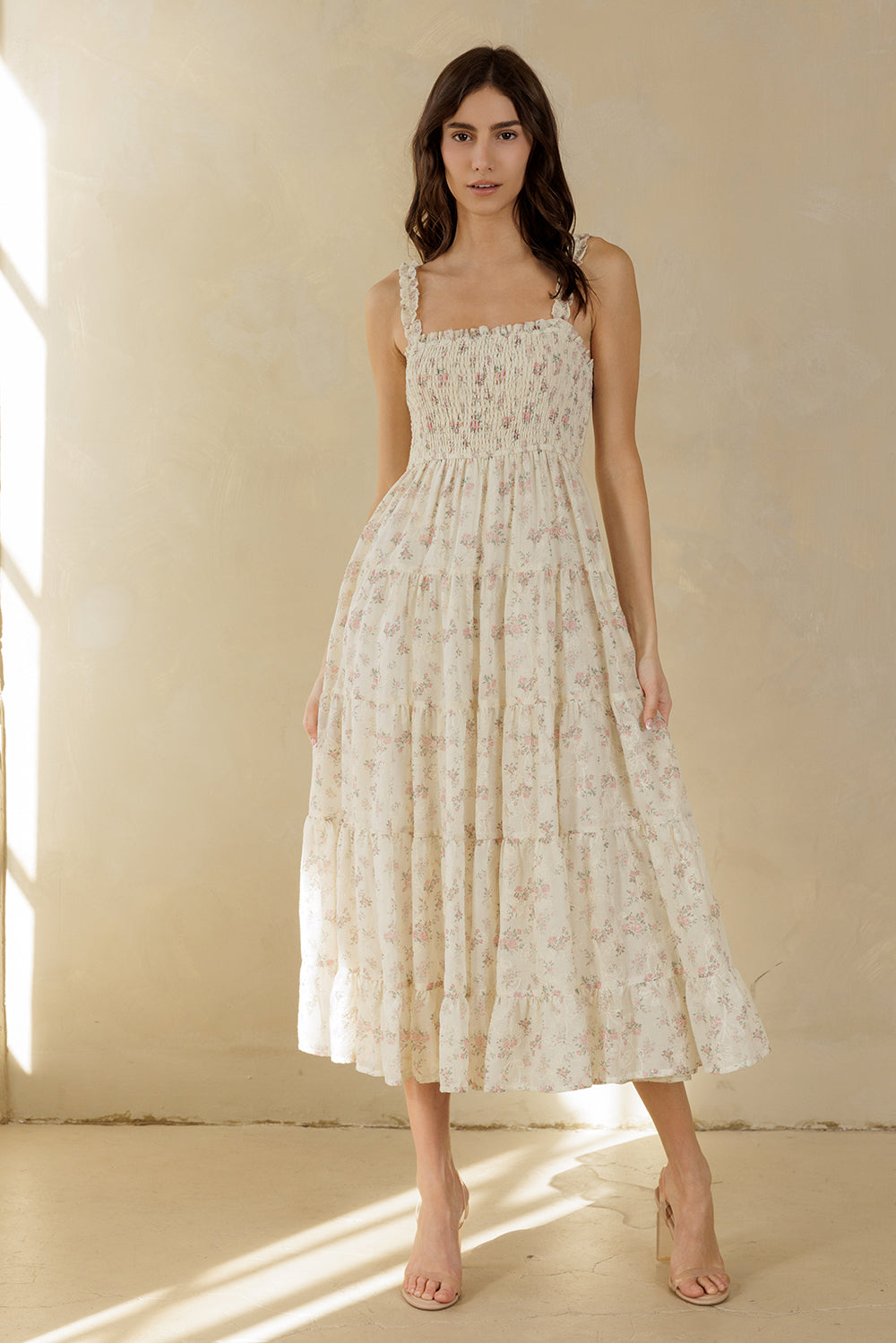 Woman wearing a cream floral dress standing in a softly lit room with a neutral background