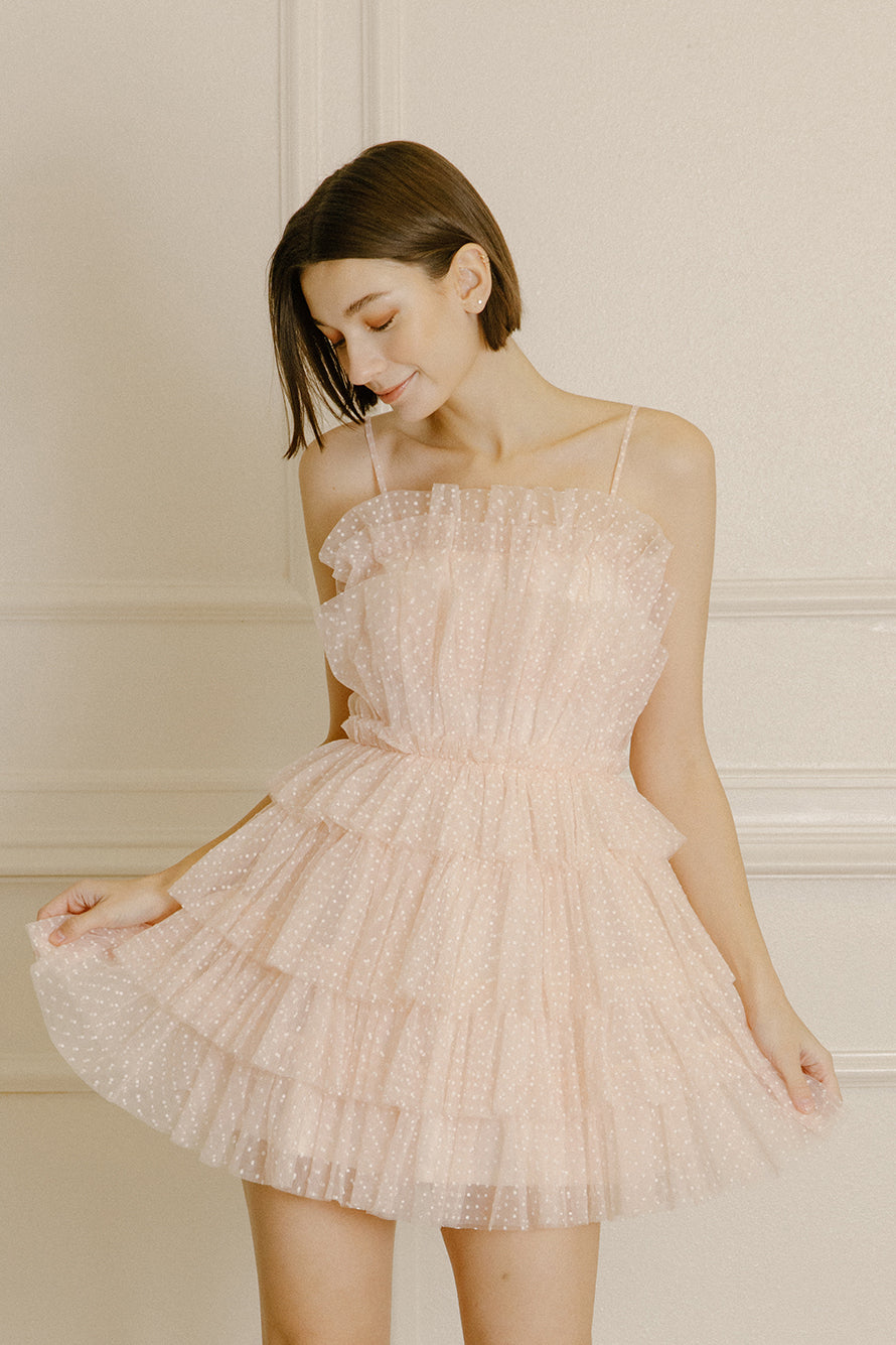 Woman wearing a soft pink mini dress with white dots and tiered tulle on a beige background