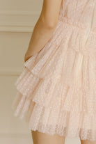 Details of a soft pink mini dress with white dots and tiered tulle on a beige background
