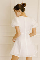 Back view of a woman wearing a white dress against a light-colored wall
