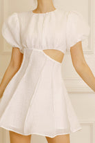 White dress with puff sleeves and cut-out design on a neutral background