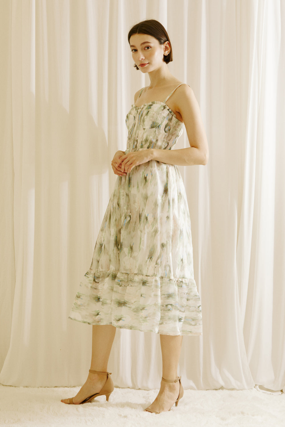 Side view of a woman wearing a green and blue tie dye effect midi dress standing against a plain background