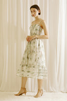Side view of a woman wearing a green and blue tie dye effect midi dress standing against a plain background