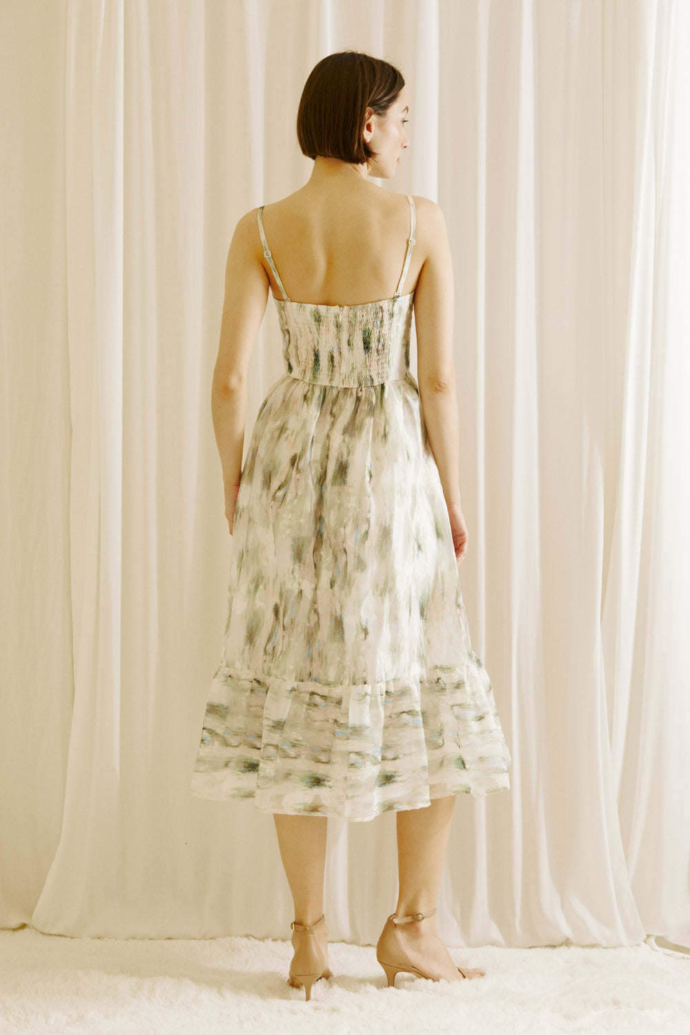 Back view of a woman wearing a green and blue tie dye effect dress standing against a plain background
