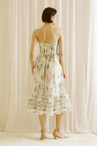 Back view of a woman wearing a green and blue tie dye effect dress standing against a plain background