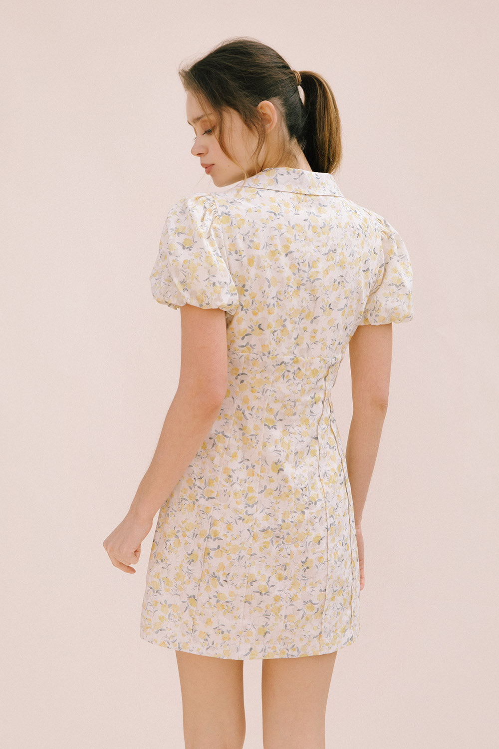 A woman viewed from behind wearing a cream dress with a floral pattern, short puff sleeves and a bodycon fitted body.