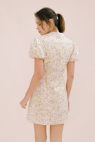 A woman viewed from behind wearing a cream dress with a floral pattern, short puff sleeves and a bodycon fitted body.