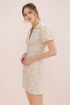 A woman modeling a cream dress with a floral pattern, short puff sleeves and a bodycon fitted body.