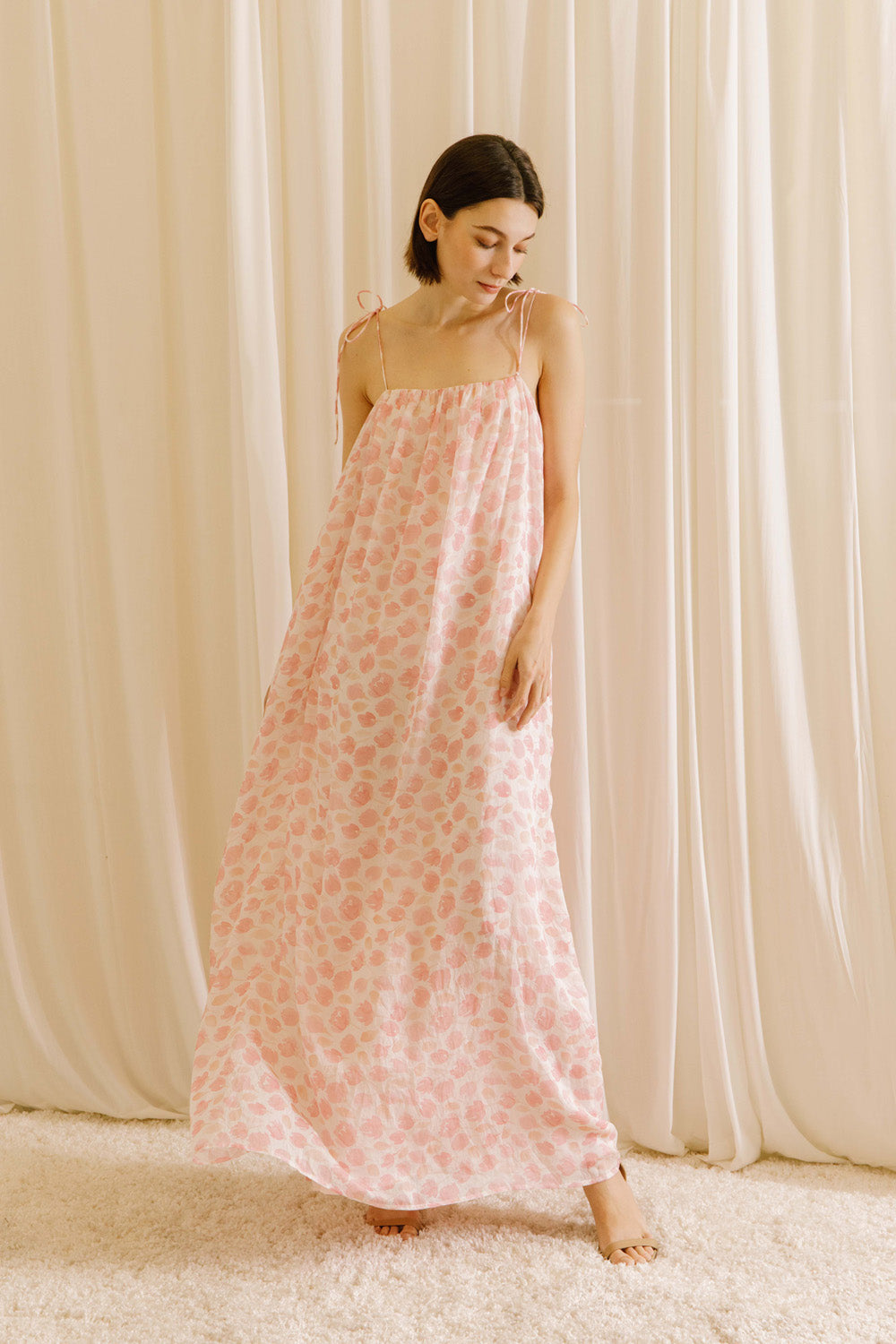 Model wearing a pink tulip floral maxi dress standing against a beige curtain.