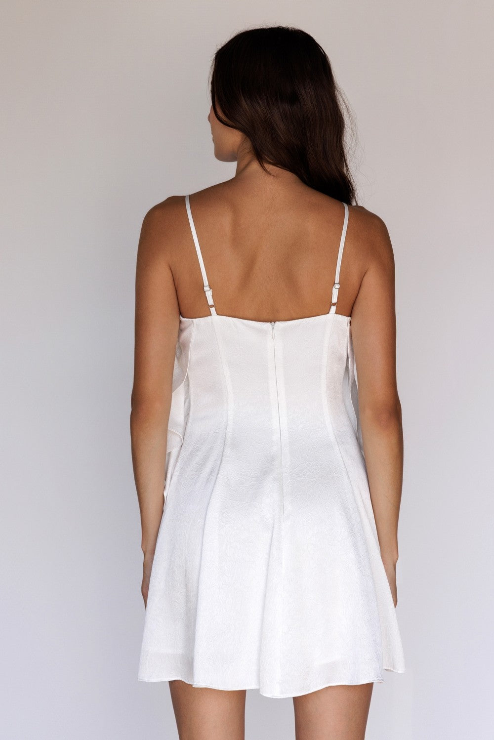 Back of a woman wearing a white slip dress against a plain background