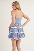 Back view a woman wearing a light blue dress with white trim on a plain background
