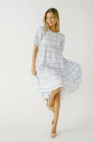 Woman in a blue checkered dress and beige high-heels against a white wall