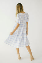 Back view of a woman in a blue checkered dress and beige high-heels against a white wall