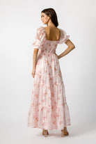 Back view of a woman wearing a pink floral dress on a white background