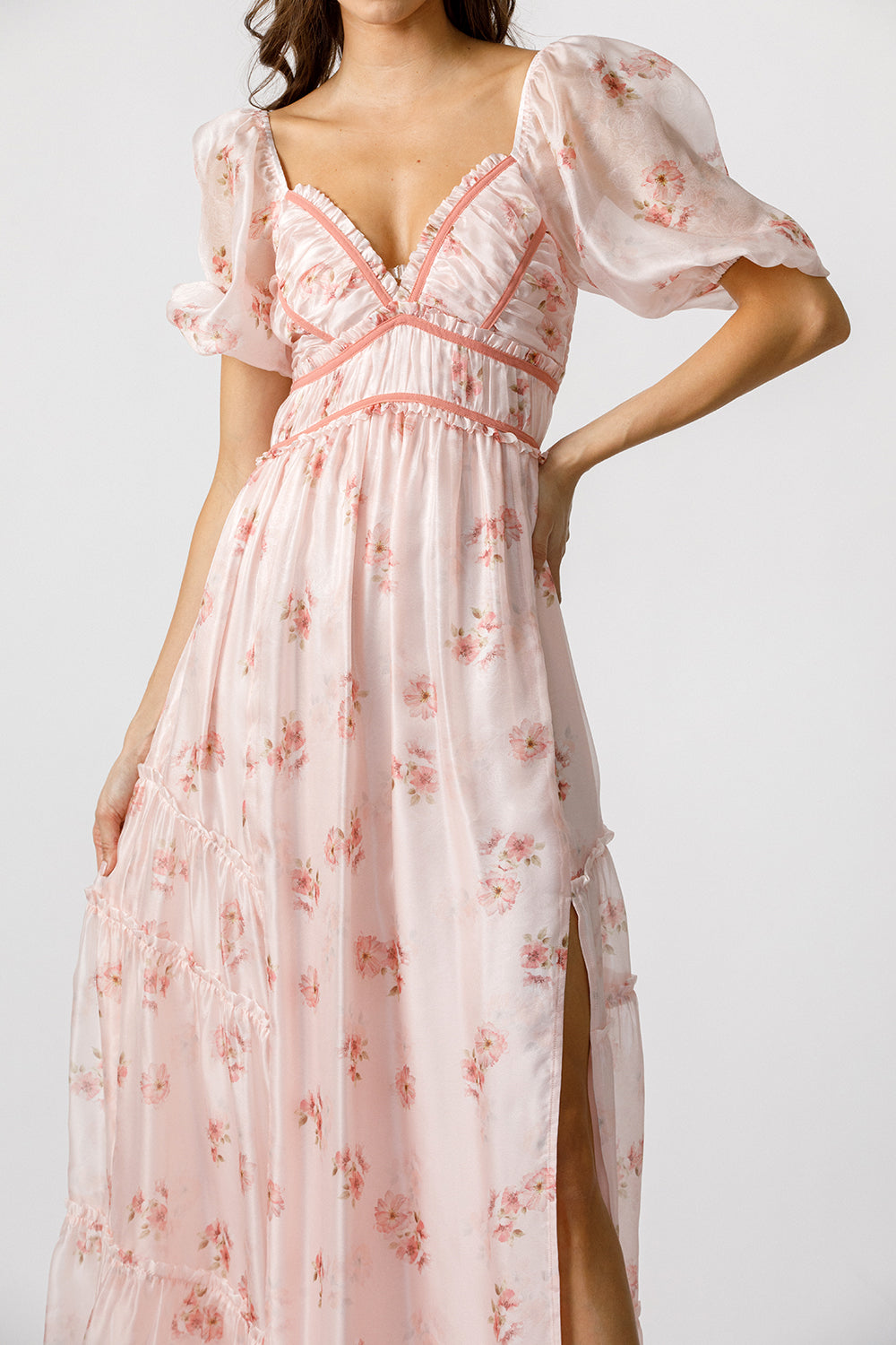 Woman wearing a pink floral dress with a side slit on a white background