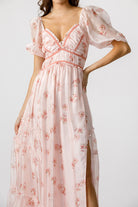 Woman wearing a pink floral dress with a side slit on a white background