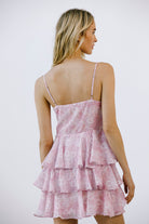 Back view of a woman wearing a pink tiered dress with thin straps on a white background