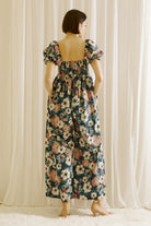 A woman viewed from behind wearing a flowy jumpsuit standing in front of white curtains