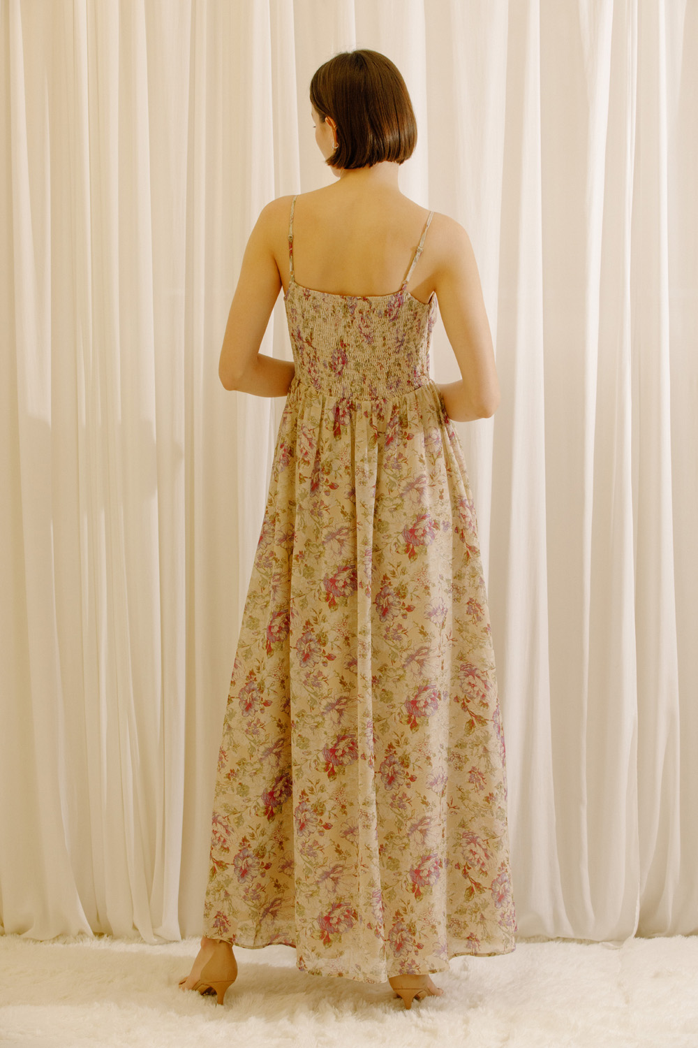 A woman viewed from behind wearing a maxi dress with a romantic floral print, adjustable straps and a flowy maxi silhouette.
