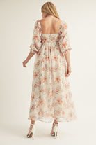 Back view of a woman wearing a beige floral dress with a plain background