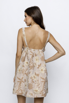 A woman viewed from behind wearing a brown and gold mini dress with shimmering floral brocade, a sweetheart neckline, and empire waist