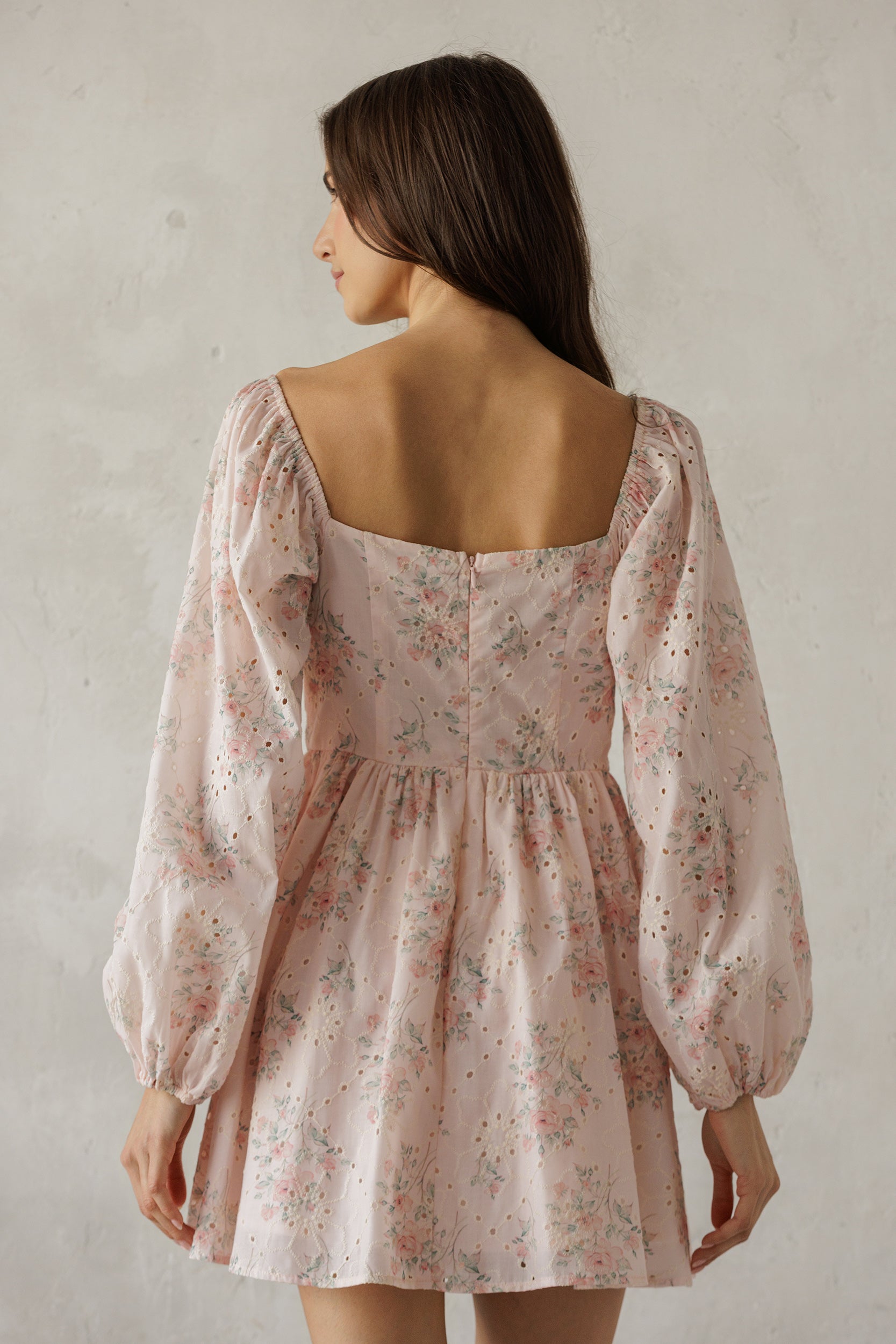 Woman wearing a floral dress with long sleeves against a plain background