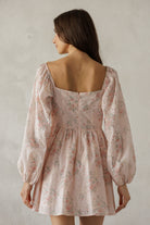 Woman wearing a floral dress with long sleeves against a plain background