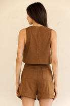 A woman shown from the back wearing a sleeveless cropped top and matching shorts in a warm brown suede-like fabric, against a plain light beige studio background.
