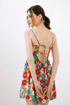 A woman wearing a colorful floral spaghetti-strap dress, shown from the back against a plain white studio background.