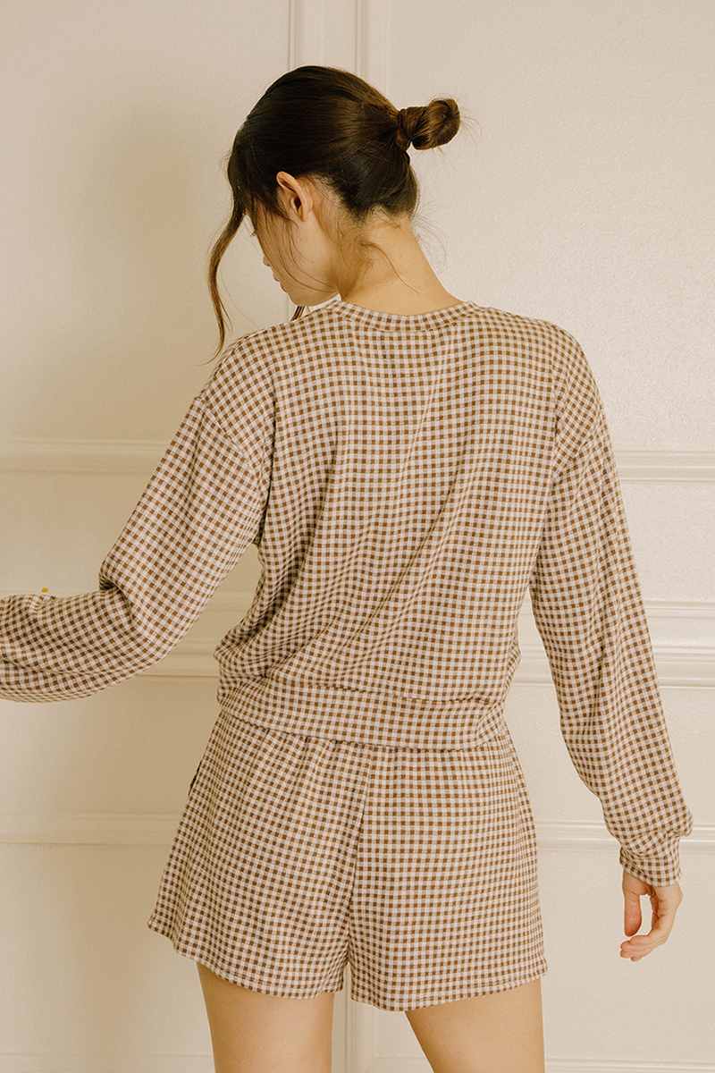 Back view of a model wearing a lounge set that features a relaxed long-sleeve top and high-waisted shorts in a brown and ivory gingham print.