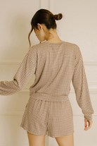 Back view of a model wearing a lounge set that features a relaxed long-sleeve top and high-waisted shorts in a brown and ivory gingham print.