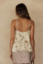 A woman viewed from behind wearing a camisole top with an ivory satin finish, vintage yellow floral print, lace-trimmed V-neckline, and flowy fit.
