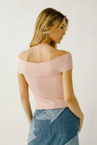 A woman viewed from behind wearing a light pink off-shoulder top and denim skirt on a plain background