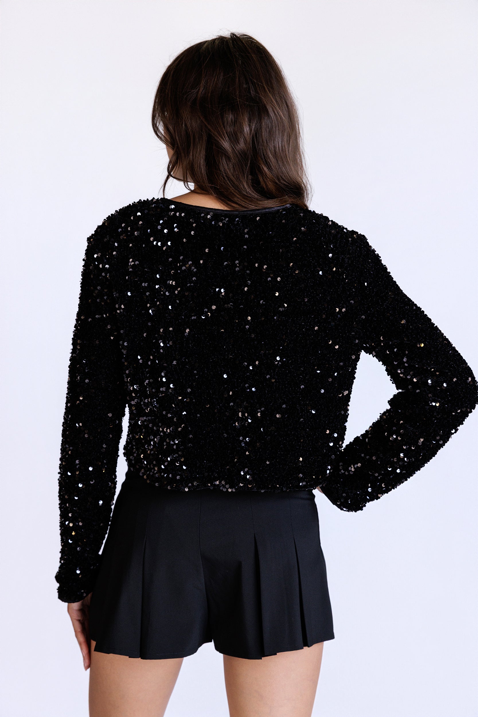 Back view of a model wearing a black sequin jacket and black shorts on a white background