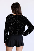 Back view of a model wearing a black sequin jacket and black shorts on a white background