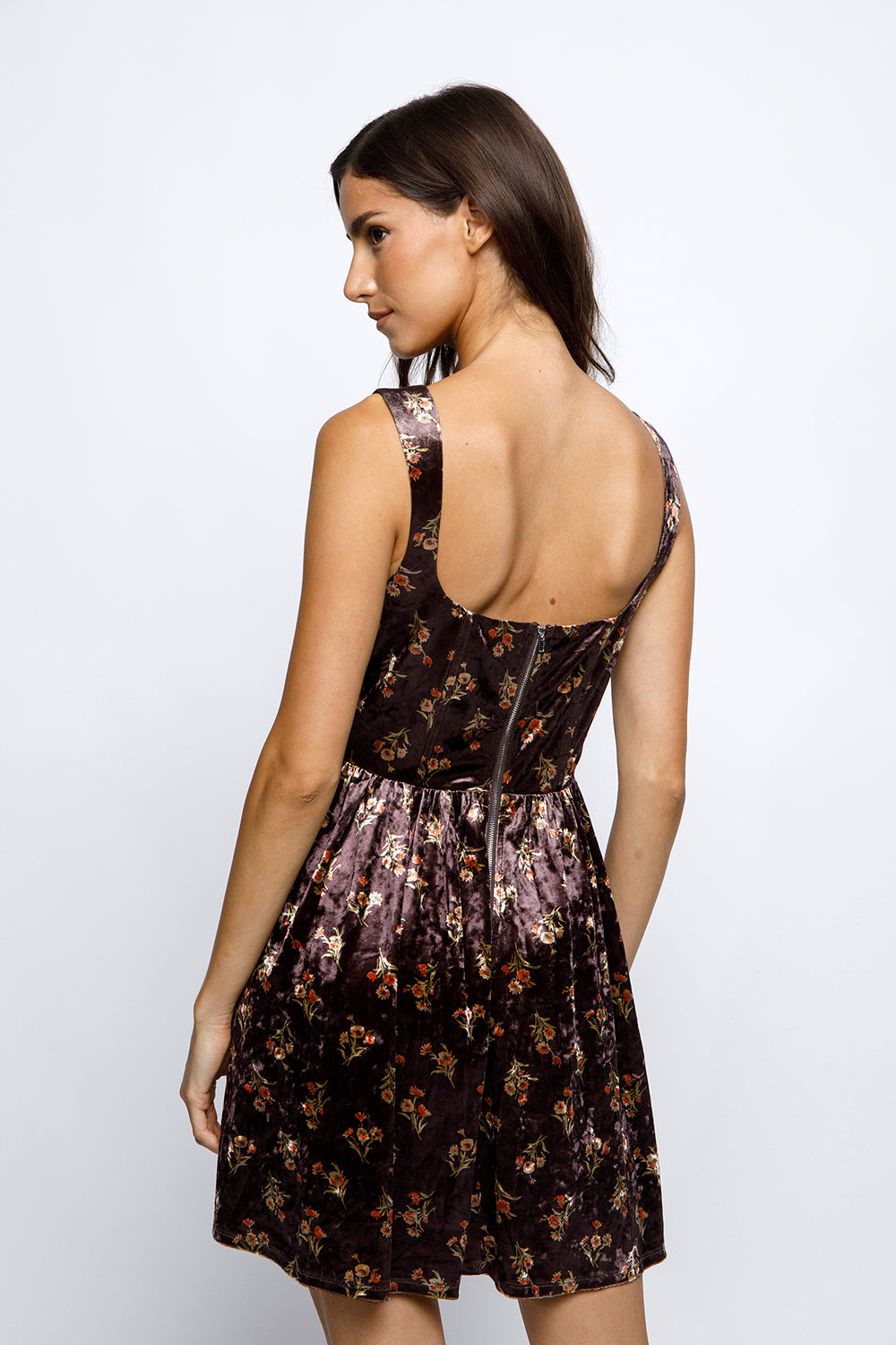 Back view of a woman wearing a brown floral velvet mini dress on a white background