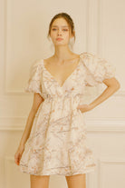 Woman wearing a cream dress with cherry blossom print against a neutral background