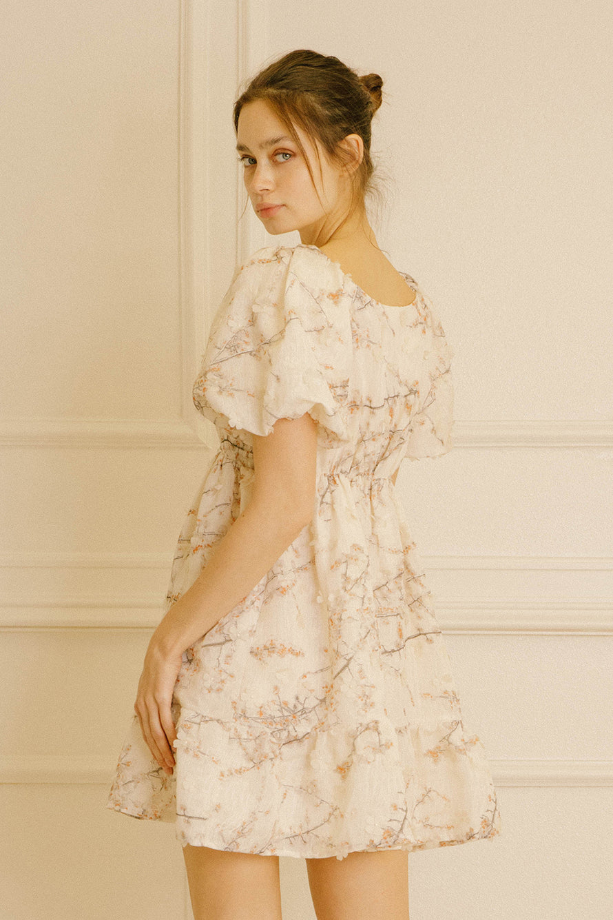 Side view of a model wearing a cream dress with cherry blossom print against a neutral background