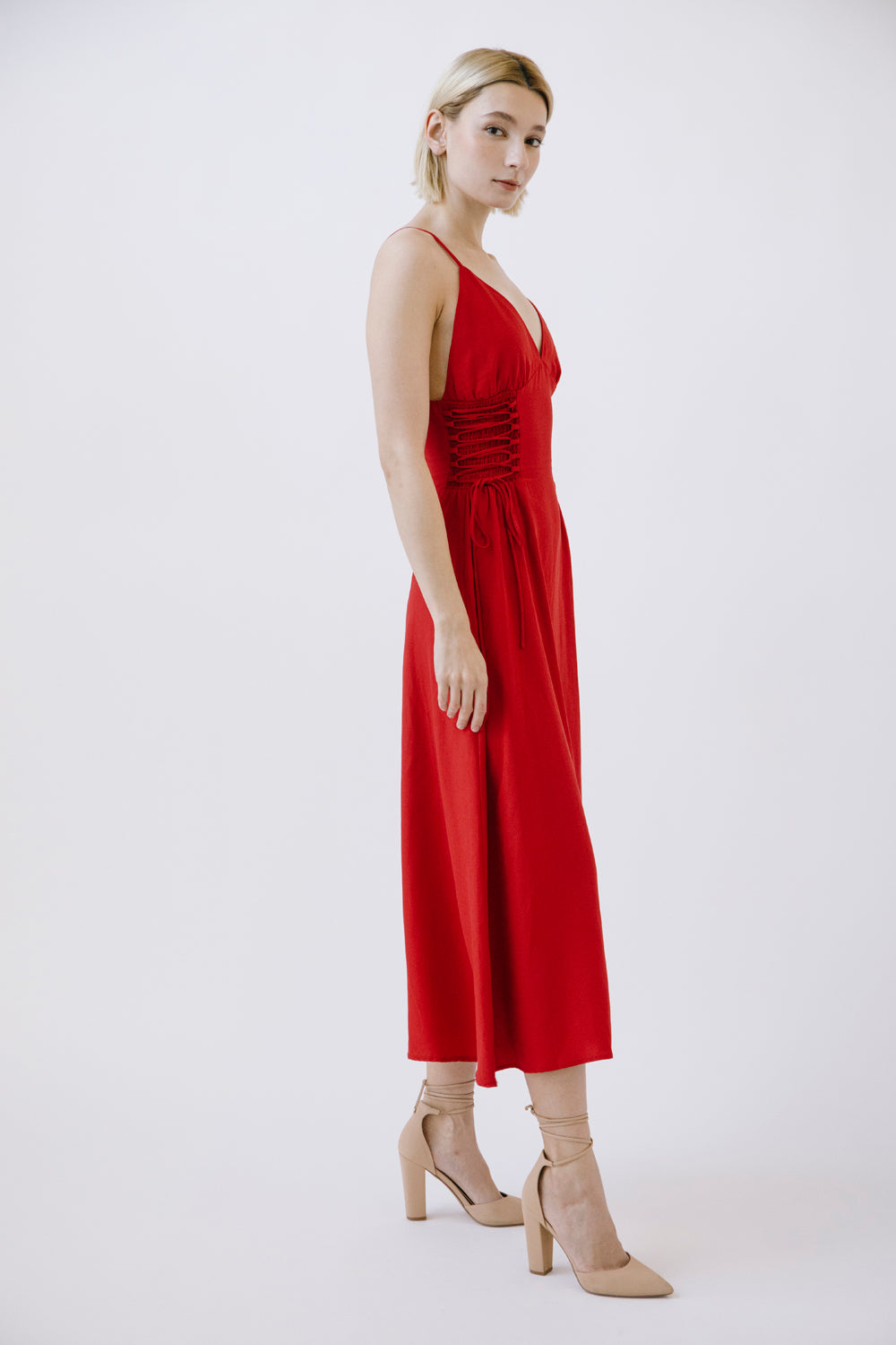 Side view of a woman wearing a red dress with beige shoes on a white background