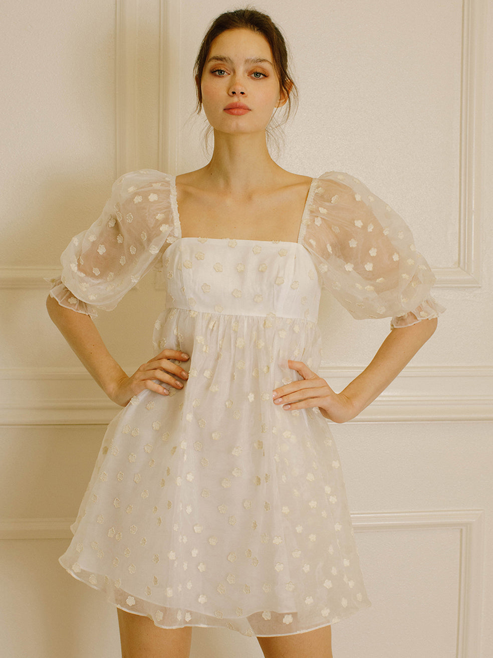 Woman in a cream polka dot dress against a neutral wall