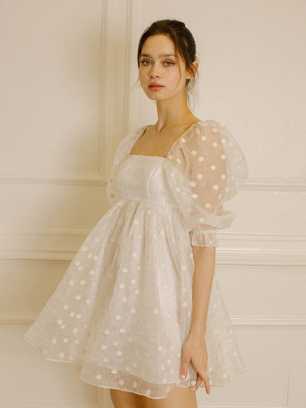 Side view of a woman in a cream polka dot dress against a neutral wall