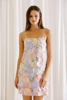 Woman wearing a floral applique dress against a white curtain background