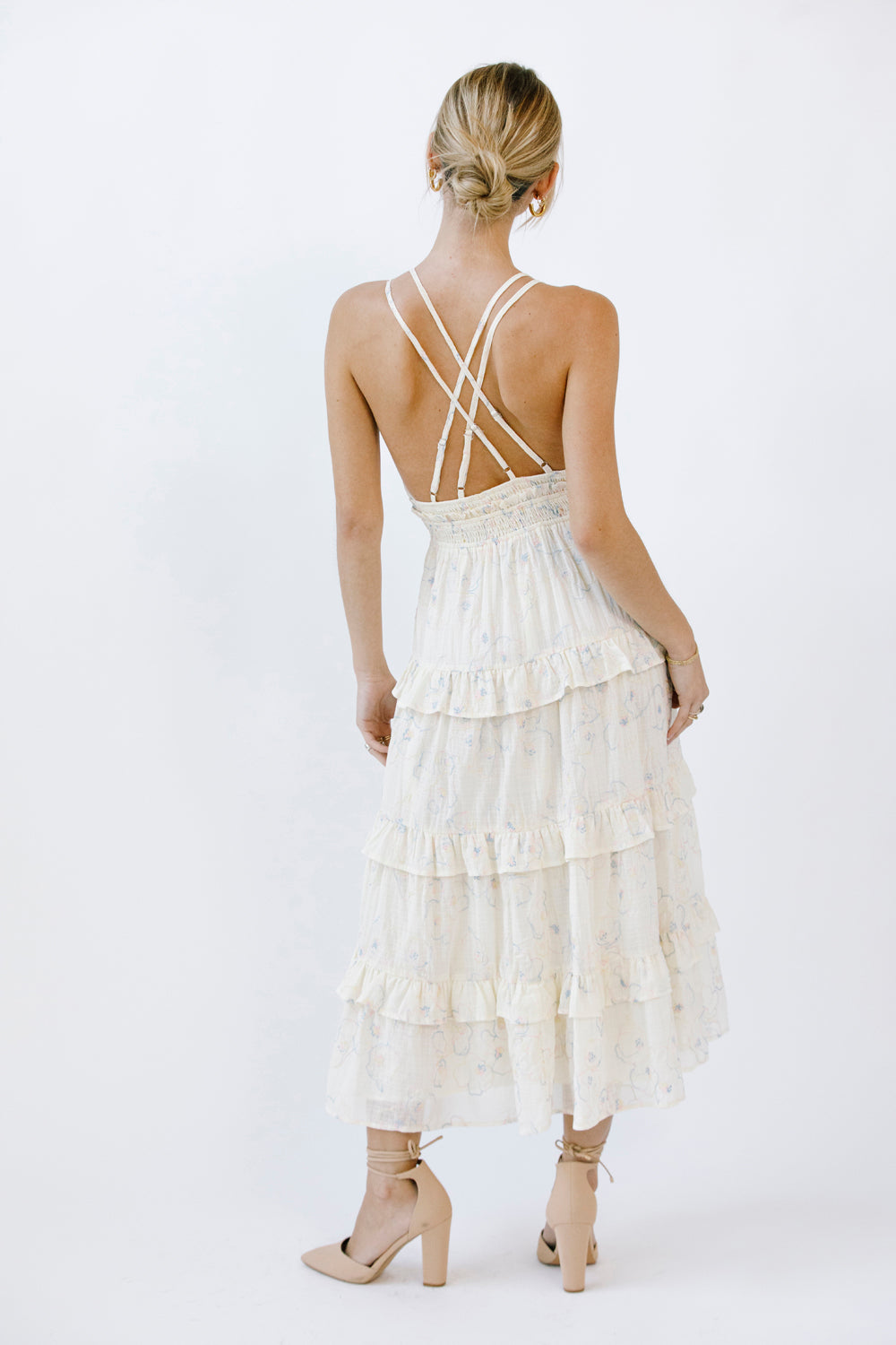 Woman wearing a cream midi dress with criss-cross straps and ruffled layers on a white background