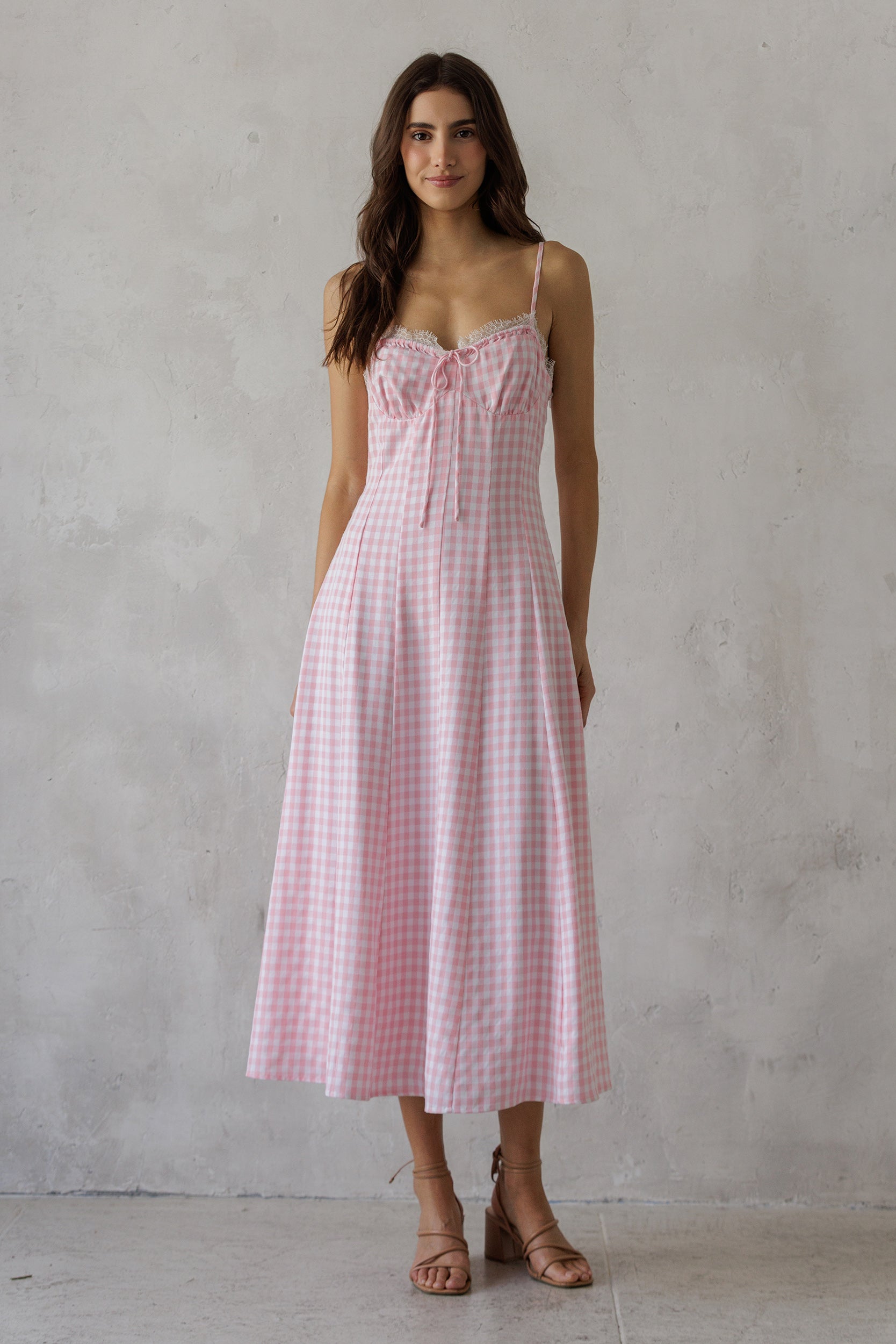 Woman wearing a soft pink gingham pattern midi dress against a grey wall