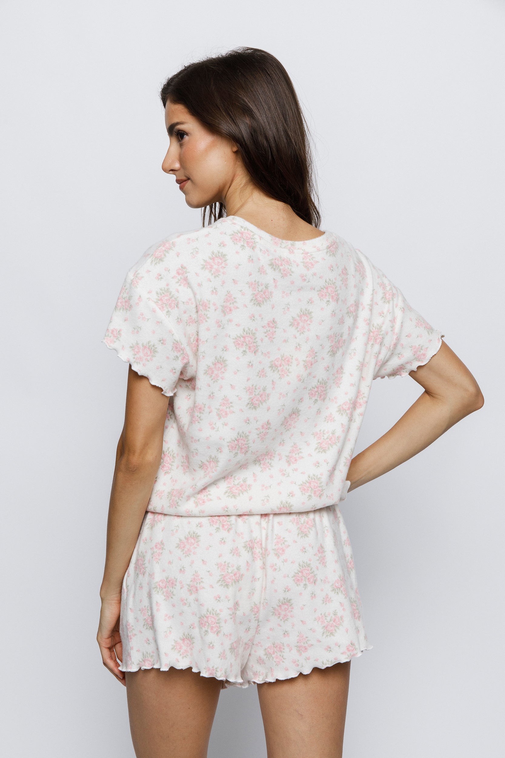 Back view of a woman wearing a light pink floral pajama set against a white background