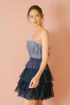 Side of a woman wearing a blue ombre tulle tiered dress against a pink background
