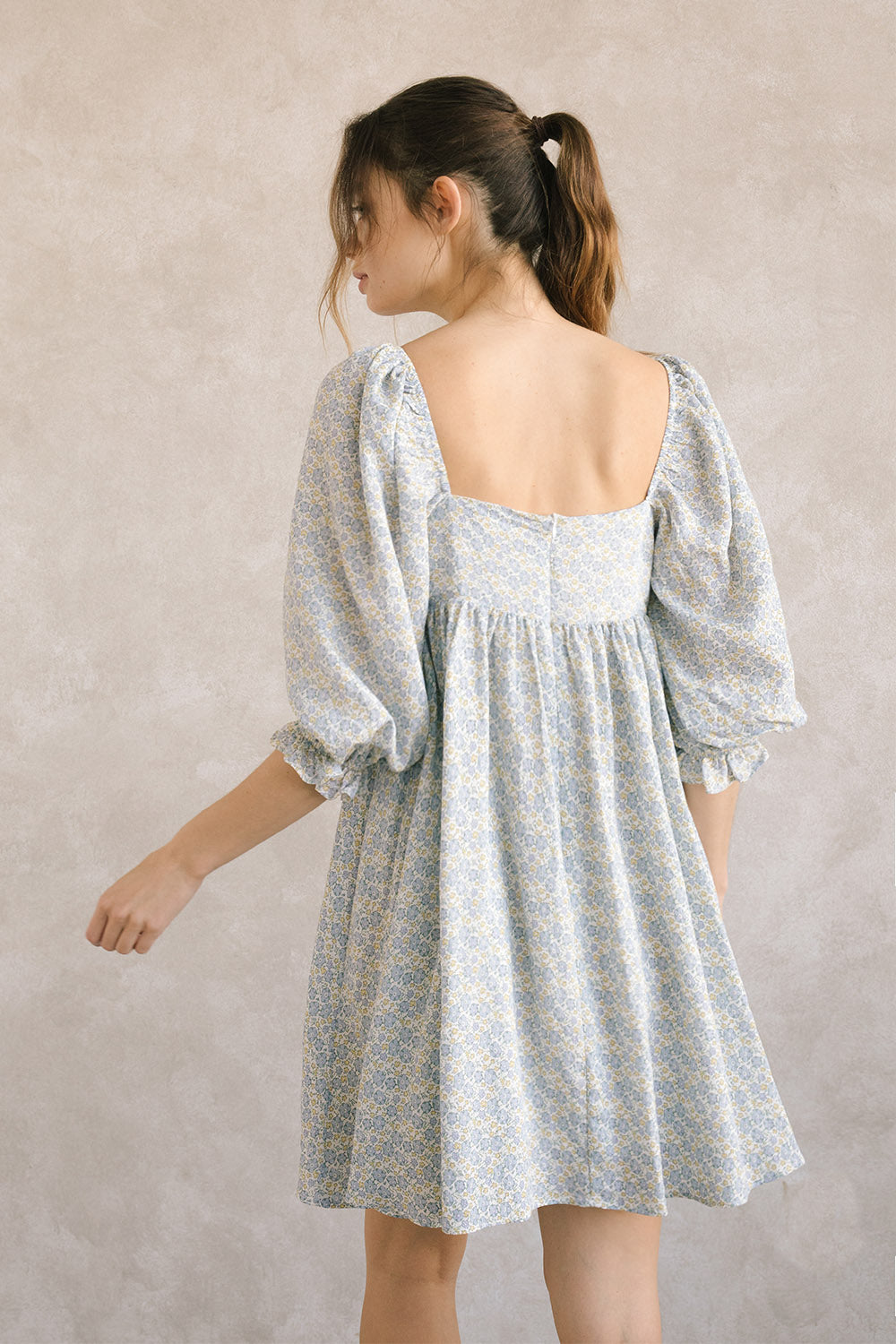 Back view of a woman wearing a blue floral dress against a plain background