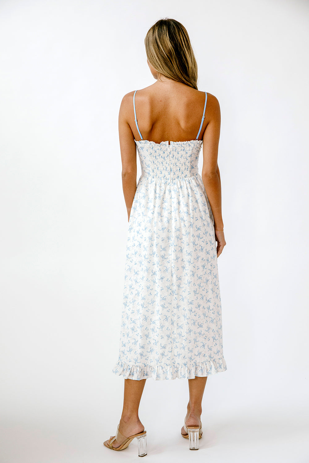 Back view of a woman wearing a white dress with blue floral patterns on a white background